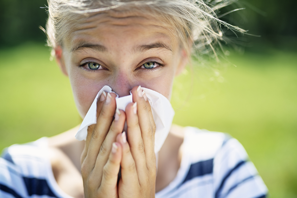 A woman with puffy eyes blows her nose outdoors during allergy season.