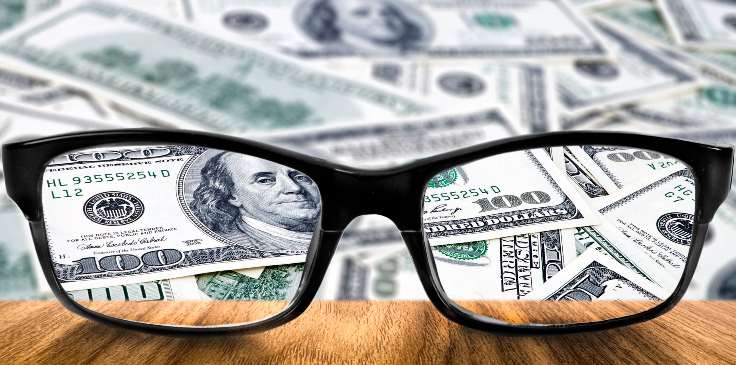 A pair of glasses rest on a table with cash visible through the lenses.